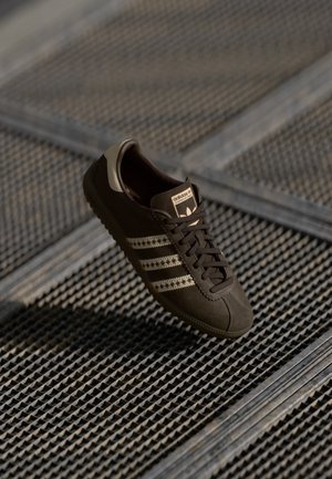 Sneaker in suede marrone con tre strisce dorate, suola in gomma e punta cucita. Presenta chiusura con lacci e logo del marchio sulla linguetta.