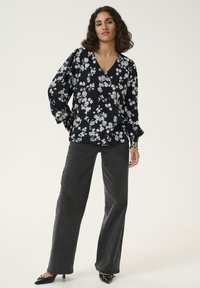 Blusa a maniche lunghe con un motivo floreale in bianco e nero, scollatura a V e maniche a sbuffo, abbinata a jeans grigi scuri a gamba larga e scarpe con tacco nere.