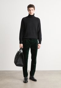 Black turtleneck sweater, green velvet pants, black leather boots, and a textured black handbag. Simple, modern design with clean lines.