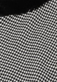 Sort-hvid houndstooth-stof med en tekstureret overflade og en glat sort kunstpelskant langs den ene kant.