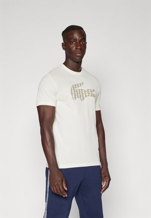 T-shirt bianco a maniche corte con un logo geometrico in oro testurizzato a forma di coccodrillo sul davanti. Design classico con collo rotondo. Tessuto di cotone morbido.