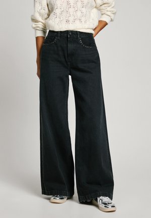 Jeans neri a gamba larga in denim con cuciture a contrasto e design a cinque tasche, abbinati a sneakers argentate.