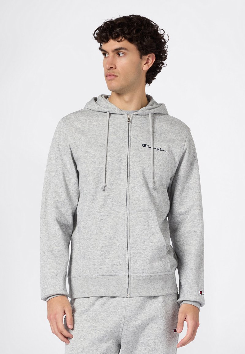 Sudadera con capucha gris y cremallera, fabricada con tela suave, que incluye capucha con cordón, bolsillos delanteros y logotipo bordado en el pecho.