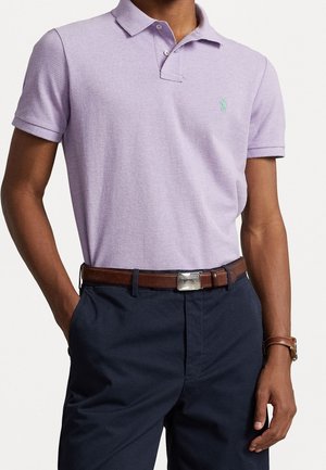 Paarse polo met een twee-knopen sluiting, korte mouwen en een geborduurd logo op de borst; gecombineerd met marineblauwe broek en een bruine riem.