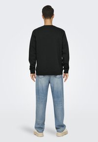 Svart sweatshirt med långa ärmar och rund halsringning, kombinerad med ljusblå, löst sittande jeans av denim och beige sneakers. Enkel design, utan grafik.
