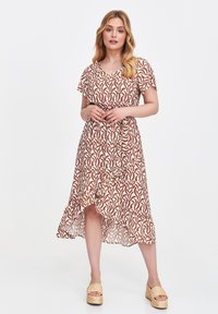 Braun- und cremefarbenes Musterkleid mit kurzen Ärmeln, einem V-Ausschnitt und einem Rüschensaum. Getragen mit Plateausandalen mit geflochtenem Design.