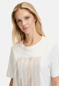 Hvid bomulds t-shirt med en glitrende "Ciao" grafisk tryk i guld- og blå rhinsten. Korte ærmer og rund halsudskæring.