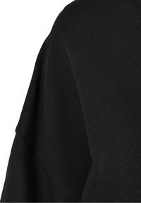 Gros plan sur un tissu noir montrant un motif tricoté texturé et la couture d'une manche de vêtement.