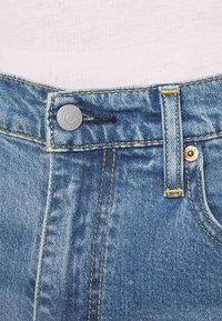 Jeans i jeansmaterial med en blekt blå färg, som har en metallknappstängning, kontrasterande gul sömnad och en ögla i midjan.