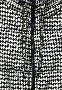 Schwarze und weiße Hahnentrittmuster-Steppjacke mit einem Reißverschluss und kontrastierenden grafischen Zugbändern. Weiches strukturiertes Material.