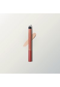 Schräger Make-up-Pinsel mit schwarz-weißen Borsten und rotem Griff, der über einem beigen Make-up-Strich auf hellem Hintergrund liegt.