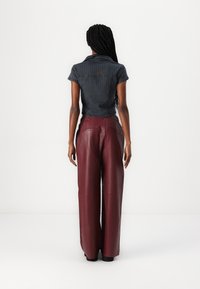 Donkergrijs gestreept shirt met korte mouwen, gecombineerd met bordeauxrode wijde leren broeken, voorzien van achterzakken en een gladde textuur.