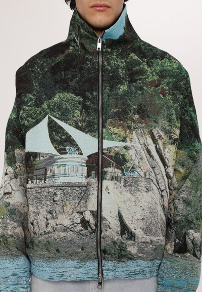 Textured zip-up jacket featuring a landscape pattern with greenery, a building, and water, primarily in shades of green, blue, and gray.