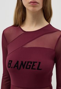 Camiseta de manga larga color burdeos, con paneles de malla transparente y un atrevido estampado en negro "B.ANGEL" en la parte frontal. Textura suave, diseño ajustado.