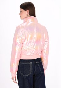 Irydyscencyjna różowa kurtka bomberka z wysokim kołnierzem i prążkowymi mankietami, charakteryzująca się błyszczącą, teksturowaną powierzchnią i elastycznym pasem.