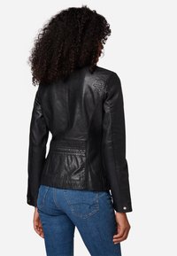 Schwarze Lederjacke mit einer taillierten Passform, die strukturierte Akzente an den Schultern und eine definierte Taille bietet. Geknöpfte Ärmelabschlüsse mit glatter Oberfläche.