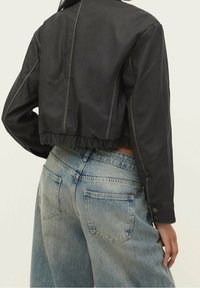 Černá krátká bunda s hladkou strukturou, s elastickým lemem. Kombinovaná s světle modrými džínami s vybledlým vzhledem.