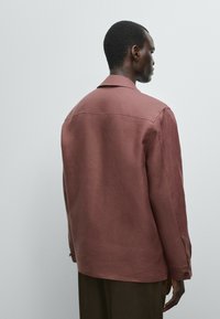 Rustkleurig linnen shirt met een rugpand, standaardkraag en lange mouwen. Het heeft knoopmanchetten en een ontspannen pasvorm, met een gladde textuur.