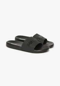 Infradito nere con una fascia larga caratterizzata da testo impresso, materiale in gomma liscia, suola piatta e design minimalista.