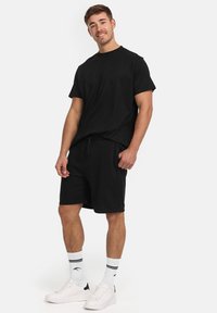 T-shirt en coton noir à manches courtes et col rond, associé à un short noir, des baskets blanches avec des accents noirs et des chaussettes rayées.