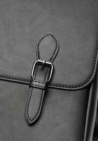 Sac en cuir noir avec une surface texturée, doté d'une boucle en métal argenté et de coutures contrastantes, mettant en valeur un design à fermeture rabat.