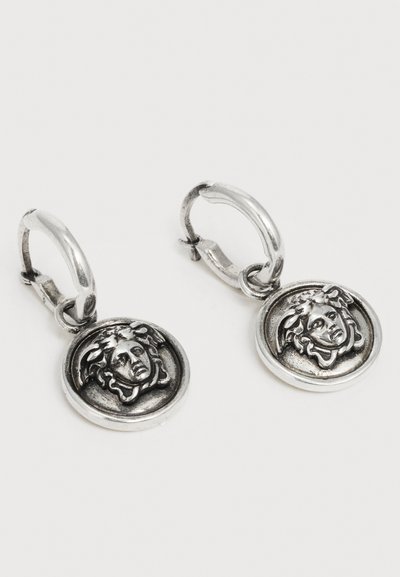 Ασημένια κρίκοι σκουλαρίκια με στρογγυλά κρεμαστά διακοσμητικά κεφαλής Μέδουσας, με λεπτομερή ανάγλυφο σχέδιο σε έναν λείο κυκλικό βάση.