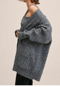 Grauer Kabelstrick-Cardigan mit offener Vorderseite, langen Ärmeln und einer Tasche. Enthält kleine dekorative Perlen im gesamten Stoff. Weiche Textur.