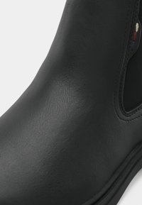 Bottines Chelsea en cuir noir avec panneau élastique sur le côté et petits détails brodés en rouge, blanc et bleu au niveau de la cheville.