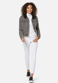 Graue Jeansjacke mit schwarzem Fleece-Kragen, Fronttaschen und Knopfverschluss, kombiniert mit einem weißen Rollkragenpullover und weißen schmal geschnittenen Hosen.