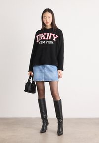 Černý pletený svetr s nápisem "DKNY NEW YORK" v červeném písmu, kombinovaný se světle modrou džínovou sukní a černými koženými bootami s vysokým podpatkem. Malá černá taška.