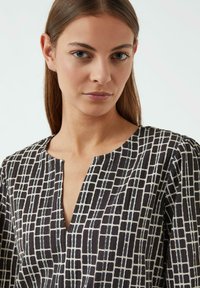 Schwarz-weiße gemusterte Bluse mit V-Ausschnitt, strukturiertem Stoff und geometrischen Quadraten im gesamten Design.