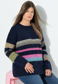 Maglione blu navy con strisce orizzontali multicolori verde, rosa e blu; texture a maglia; collo a giro. Indossato con jeans blu.