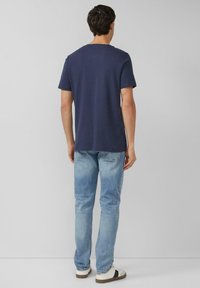 Marineblauw katoenen T-shirt met korte mouwen, ronde hals en een losse pasvorm, gecombineerd met lichtblauwe jeans en witte sneakers.