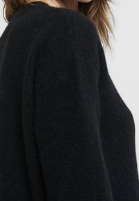 Maglione nero in lana con una finitura morbida e testurizzata. Il design presenta un ampio scollo e maniche lunghe.