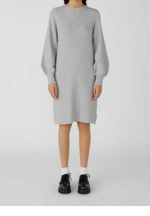 Abito grigio a maglia con un motivo a diamante testurizzato, vestibilità rilassata e maniche lunghe e svasate, abbinato a scarpe platform nere e calzini bianchi.
