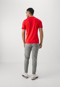 Camiseta corta roja de manga corta con escote redondo, combinada con pantalones de chándal grises. El calzado incluye zapatillas blancas con detalles en negro.