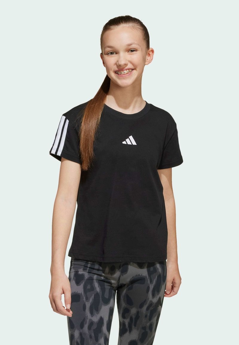 T-shirt en coton noir avec logo Adidas blanc et trois rayures horizontales sur la manche gauche, associé à des leggings à motifs noir et gris.