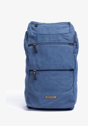 Blauer Canvas-Rucksack mit zwei schwarzen Reißverschlusstaschen, subtiler Textur und einem kleinen Metall-Brand-Tag an der unteren Vorderseite.