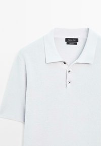Polo shirt grigio chiaro realizzato in 100% cotone, con colletto a coste, patta con tre bottoni e tessuto a maglia testurizzato.