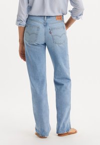 Jeans rectos de color azul claro con un diseño clásico de cinco bolsillos. Presenta un parche de cuero con la marca en la parte trasera de la cinturilla y costuras visibles.