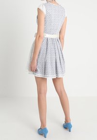 Robe fleurie bleu et blanc avec un corsage ajusté, une jupe évasée, une bordure en dentelle et une ceinture blanche, assortie à des talons bleus.