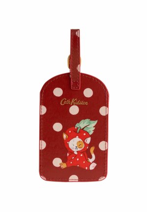 Etichetă de bagaj roșie cu buline albe, logo-ul Cath Kidston și ilustrație cu o pisică îmbrăcată în costum de căpșună cu o frunză verde deasupra.