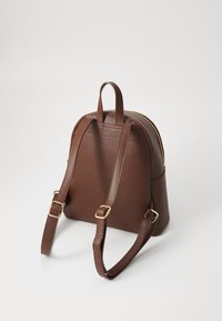 Zaino in finta pelle marrone con hardware dorato, forma arrotondata, spallacci regolabili e manico superiore per il trasporto. Chiusura con zip nella parte superiore.