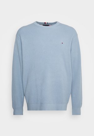 Pull tricot texturé bleu clair à manches longues avec petit logo rouge, blanc et bleu sur le côté gauche de la poitrine.