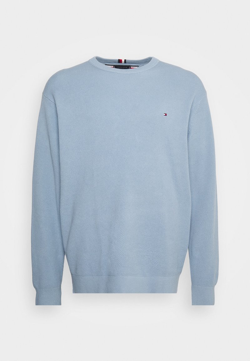 Pull tricot texturé bleu clair à manches longues avec petit logo rouge, blanc et bleu sur le côté gauche de la poitrine.