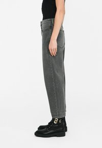 Jeans grigi alti in vita con una vestibilità ampia e orlo sdrucito, abbinati a stivali neri sopra la caviglia con un accentuato fermaglio dorato.
