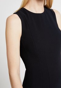 Svart ärmlös klänning med åtsittande design, strukturerad tyg och rena linjer, som visar en jämn textur utan synliga mönster.