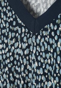 Material de marină cu o dispersie de puncte albastre deschise, verzi și albe. Are un decolteu în v și o textură moale, potrivit pentru îmbrăcăminte casuală.