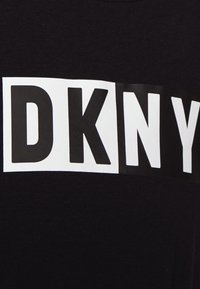 Czarny T-shirt z wyraźnymi białymi literami blokowymi tworzącymi napis "DKNY" na wysokości klatki piersiowej. Materiał wydaje się gładki, z okrągłym dekoltem.
