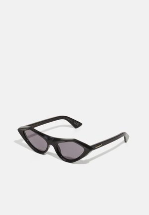 Occhiali da sole a forma di cat-eye neri con montatura angolare, lenti scure e dettagli del logo in oro sulle tempie. Materiale in plastica liscio e lucido.